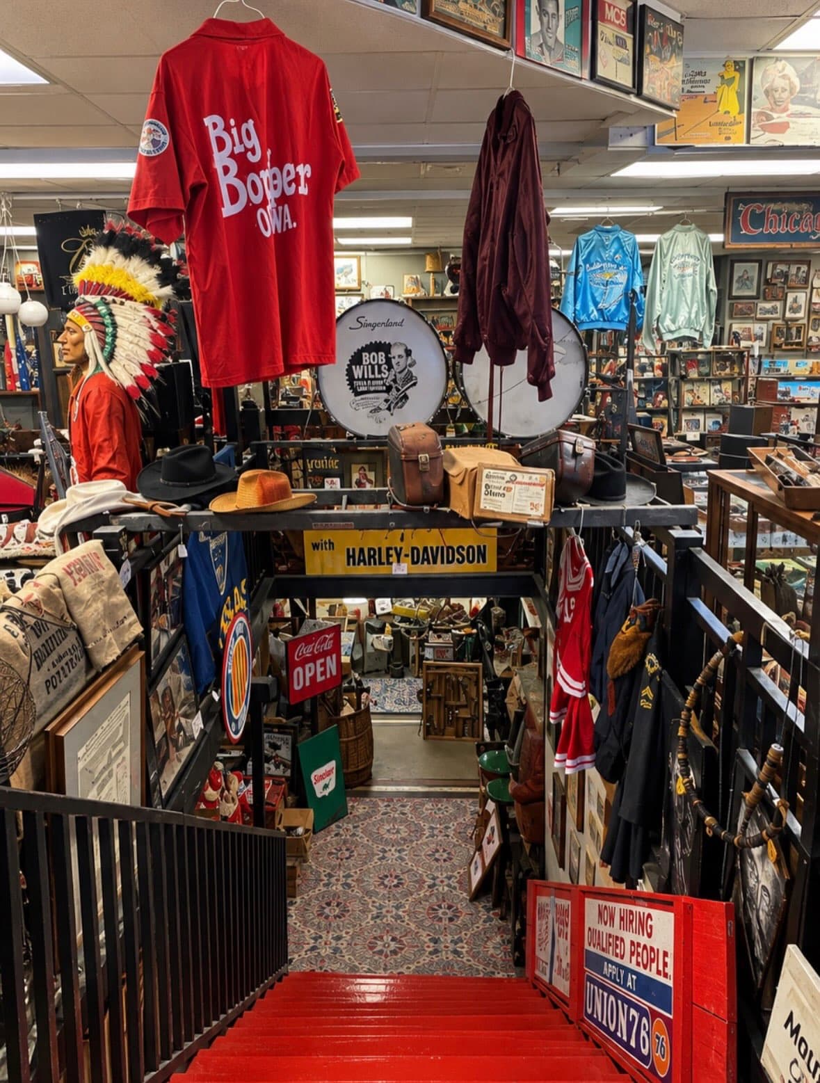 Red staircase leading into Vintage Finds Antiques in Wichita, lined with vintage signs, jerseys and a Harley-Davidson banner